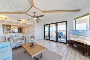 Un salon spacieux doté d’un ventilateur de plafond, d’un grand téléviseur et offrant une vue sur la plage grâce à ses portes-fenêtres coulissantes.