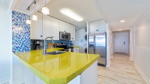 Uma cozinha moderna com bancada amarela, eletrodomésticos de aço inoxidável e painel de azulejos.