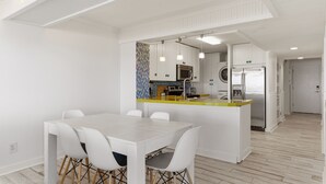 Uma cozinha moderna com armários brancos, uma ilha central e uma área de jantar com mesa e cadeiras brancas.