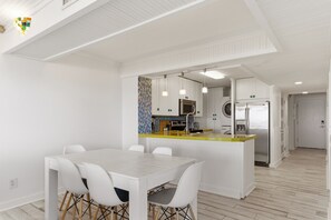 Une cuisine moderne avec des meubles blancs, un îlot central et un coin repas comprenant une table et des chaises blanches.
