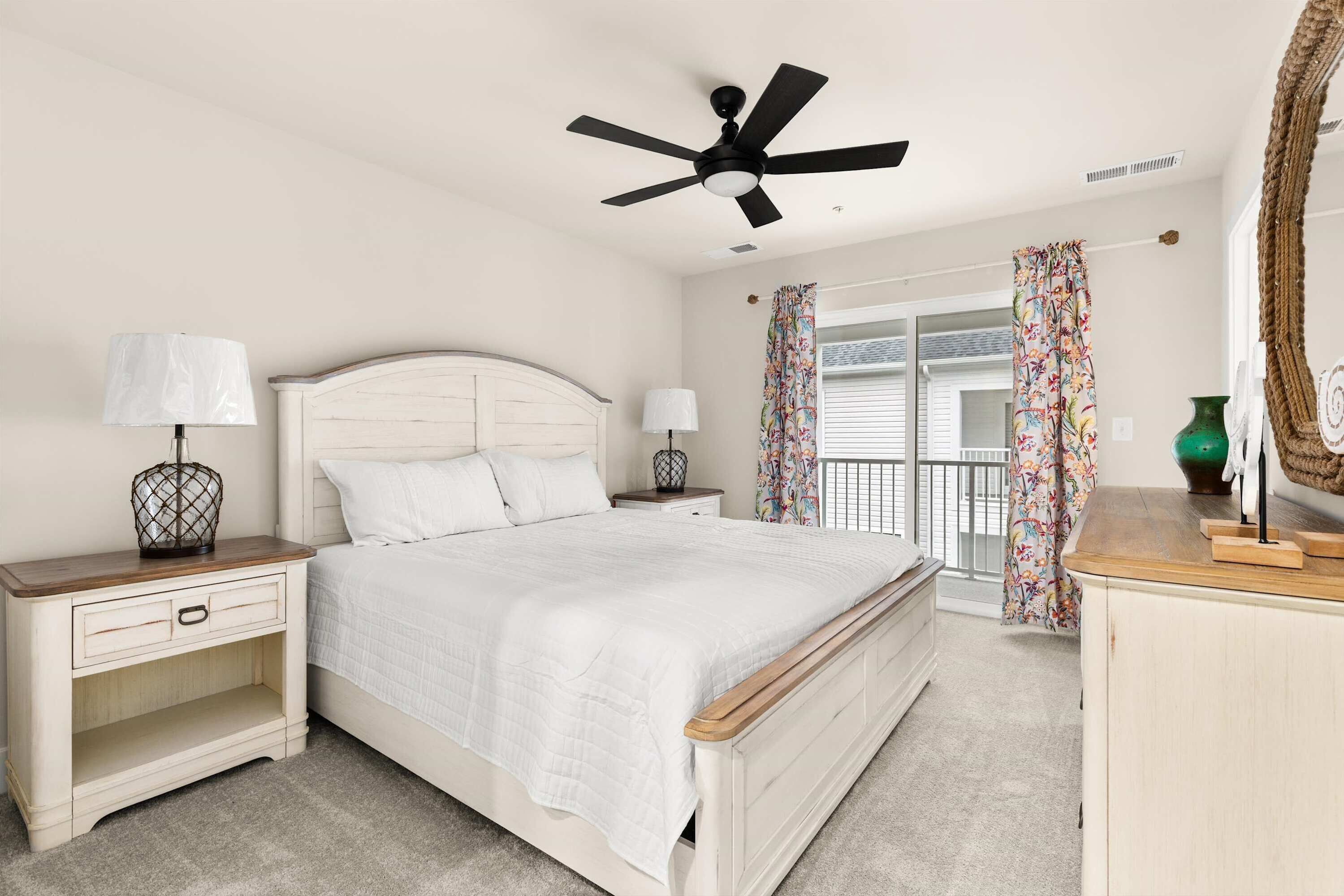 A bedroom with a bed, nightstands, a ceiling fan, a window with curtains, and a dresser.