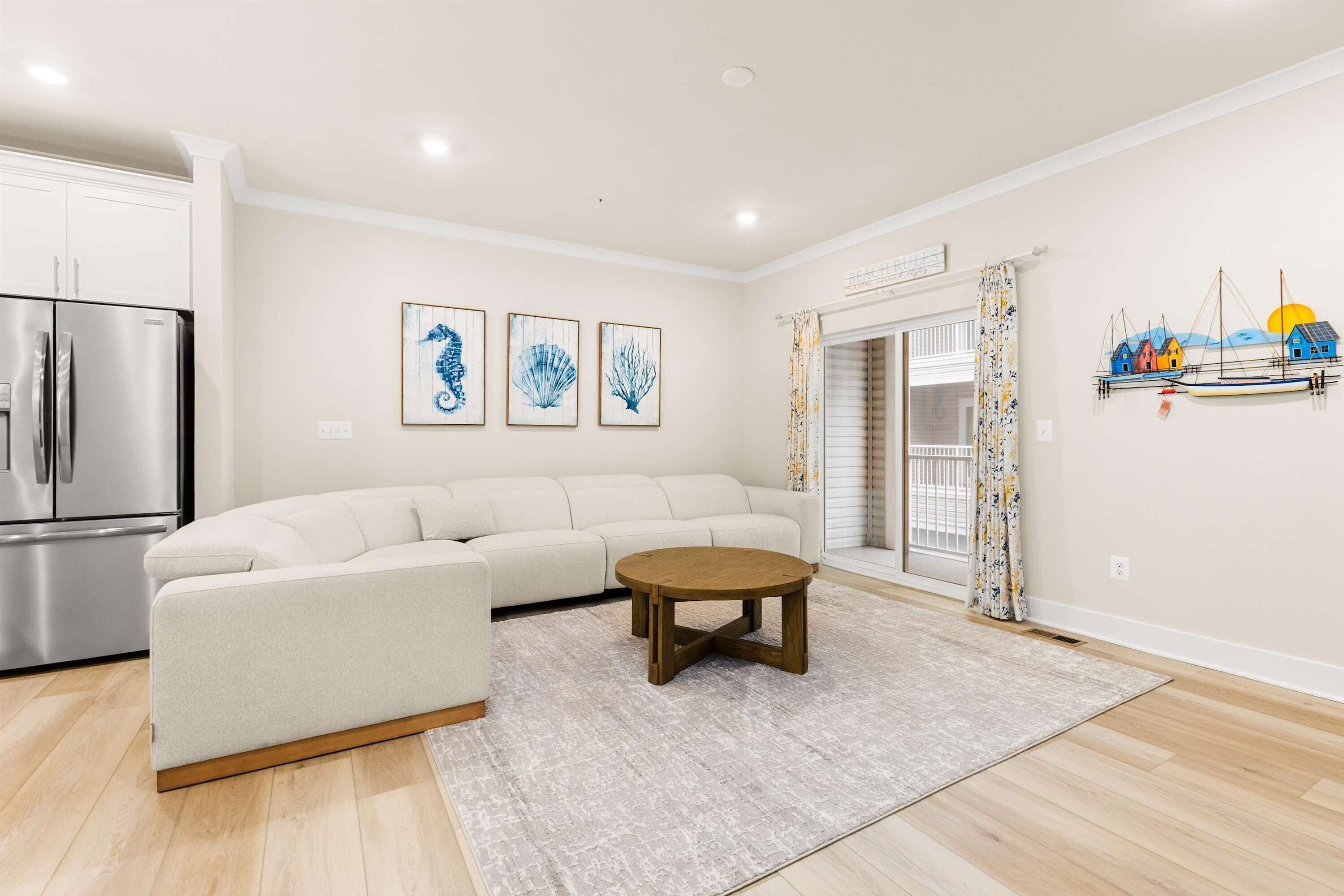 A modern living room with a sectional sofa, a wooden coffee table, and a kitchen area with a stainless steel refrigerator.