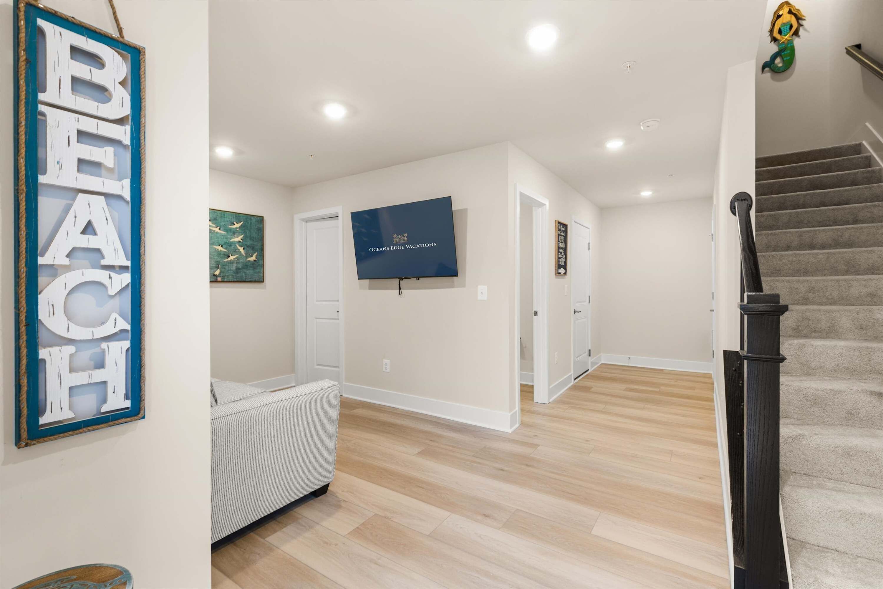 Un hall d’entrée spacieux avec un plancher en bois, un téléviseur fixé au mur et un escalier doté d’une rampe noire.