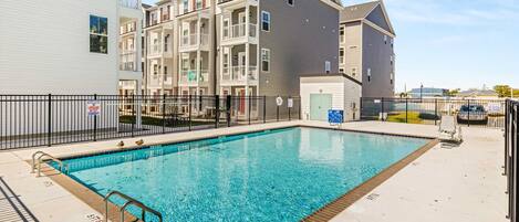 A swimming pool with a metal safety fence, adjacent to multi-story residential buildings.