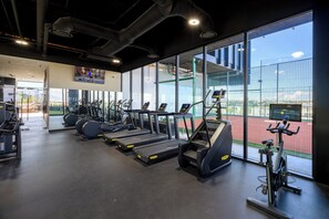 A gym with treadmills, elliptical machines, and a rowing machine, with large windows and a view of an outdoor area.