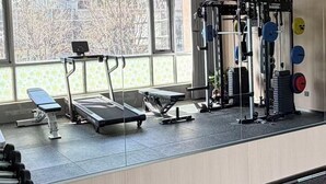 Een sportschool met loopband, gewichtbank en diverse fitnessapparaten.