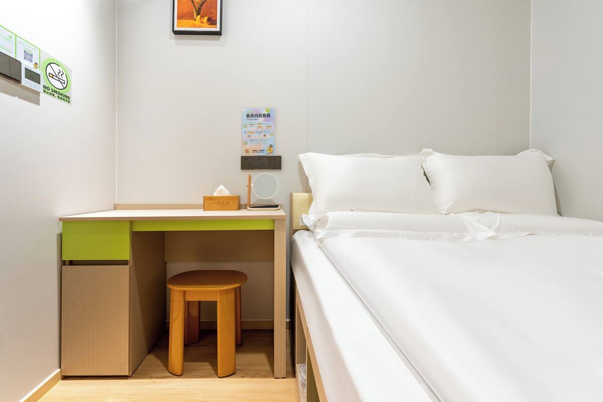 Une chambre bien rangée, avec un lit, un bureau et une chaise, ainsi qu’un petit tabouret.