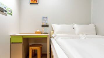 Un dormitorio ordenado con una cama, un escritorio con una silla y un taburete pequeño.