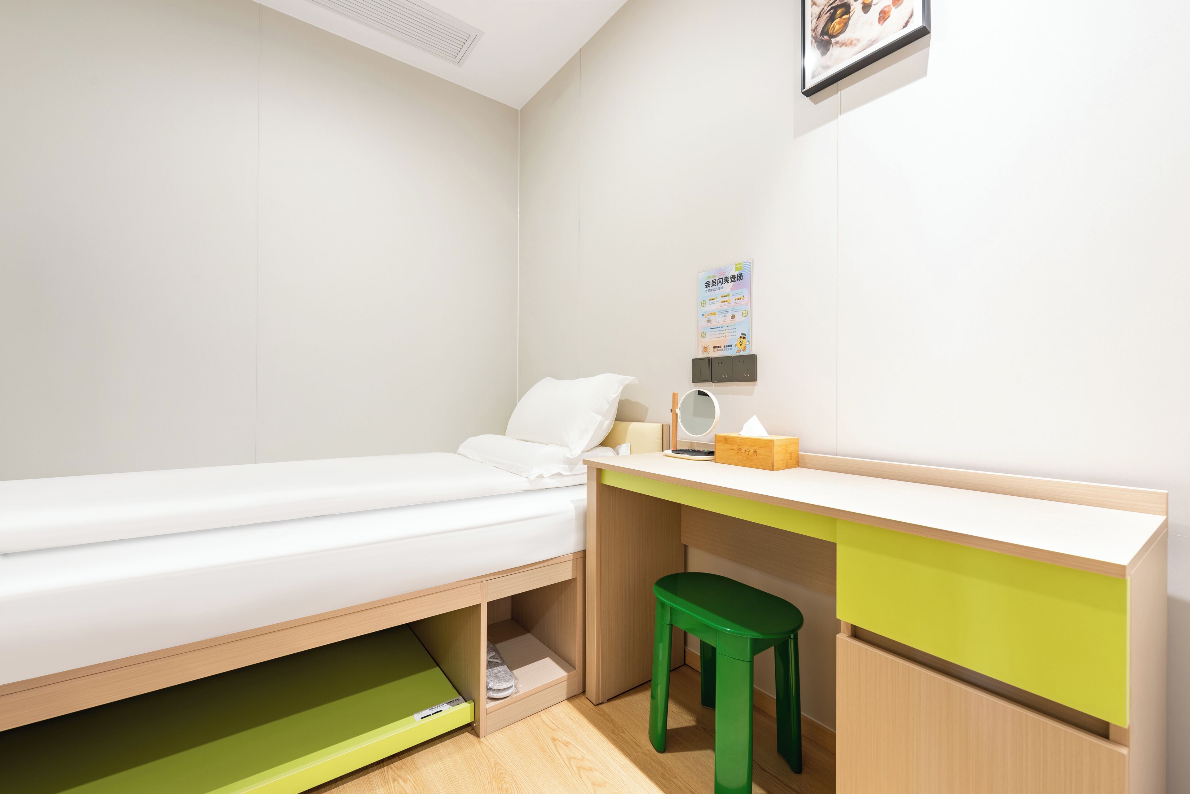 A small, neatly arranged room with a single bed, a desk with a chair, and a small shelf.