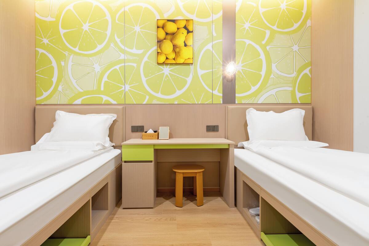 Une chambre avec deux lits, un bureau, un tabouret et un mur orné d’un motif citron.