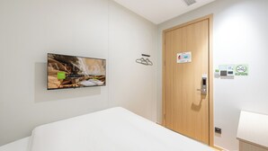 Een hotelkamer met een bed, een aan de muur bevestigde televisie, een houten deur en een rookverbodsbedekking.