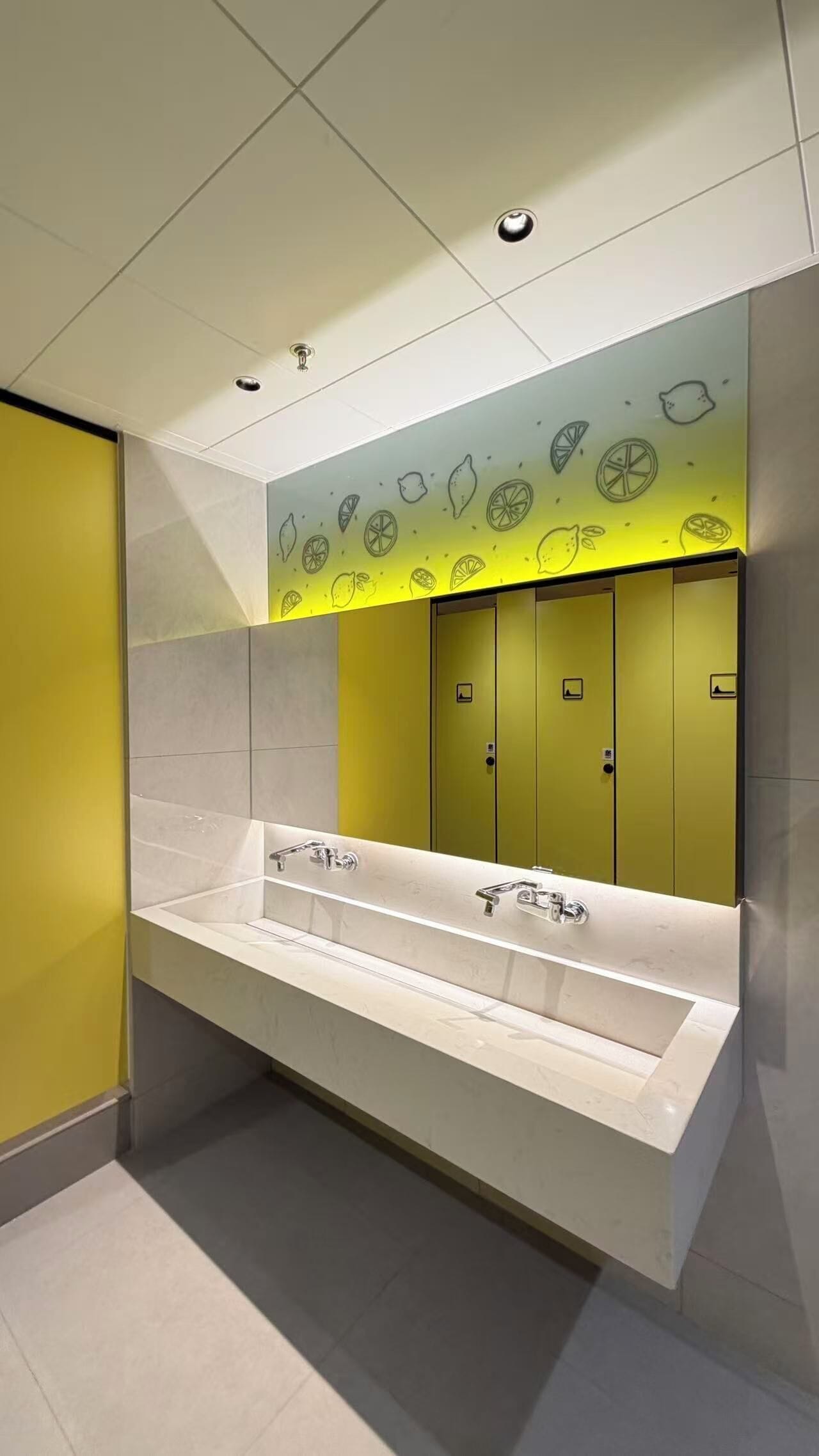 Ein modernes Badezimmer mit einem großen Waschbecken, gelben Schließfächern und einer Wand mit Zitronen-Illustrationen.