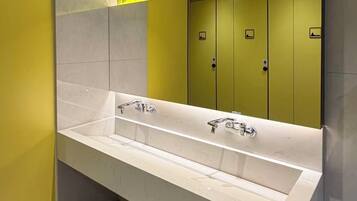 A modern bathroom with a large sink, yellow lockers, and a wall with lemon illustrations.