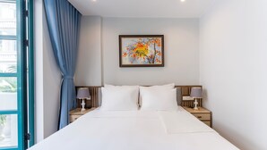 Una habitación de hotel con una cama, dos mesitas de noche con lámparas, una ventana con cortinas azules y una obra de arte enmarcada en la pared.