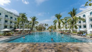 Una piscina grande rodeada de palmeras y edificios blancos con balcones.