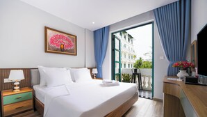 Habitación de hotel con una cama grande, un escritorio con computadora, una ventana con cortinas azules y un cuadro de un árbol.