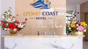 Un mostrador de recepción en el Hotel Leono Coast con un diseño de mármol y un logotipo encima.
