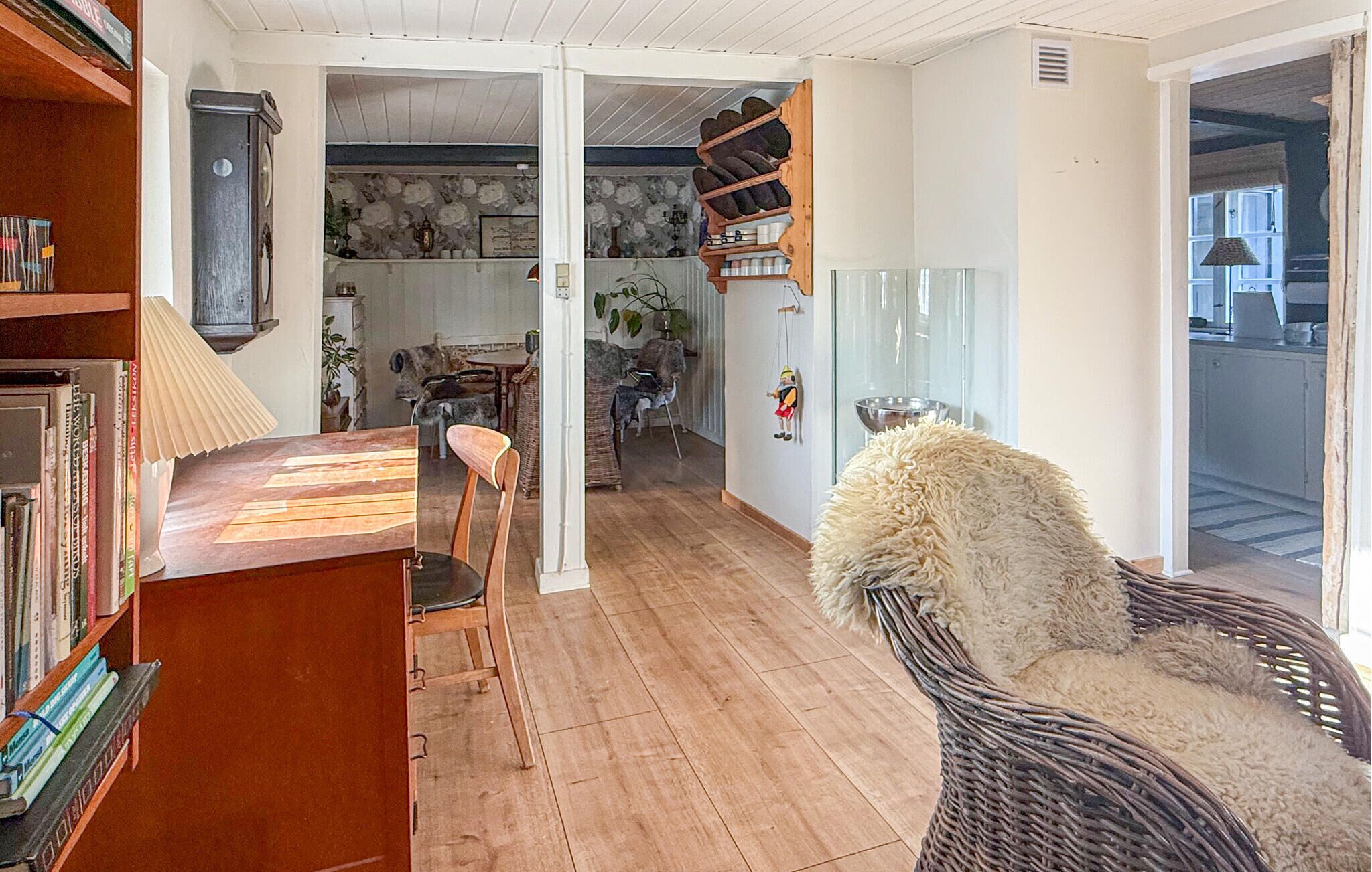 A cozy living room with a wooden floor, a bookshelf, a dining area with a table and chairs, and a wicker chair.