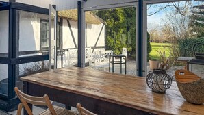 A wooden table with chairs, a woven basket, and a metal candle holder in a room with large windows and a view of a garden. - Lovely home in Nørreballe with WiFi (Nørreballe)