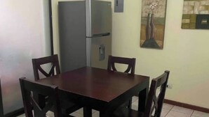 Een eetruimte met een donker houten tafel en stoelen, een koelkast, en twee schilderijen aan de muur.