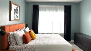 Een slaapkamer met een bed, een plafondventilator, een raam met gordijnen en een ingelijste foto aan de muur.