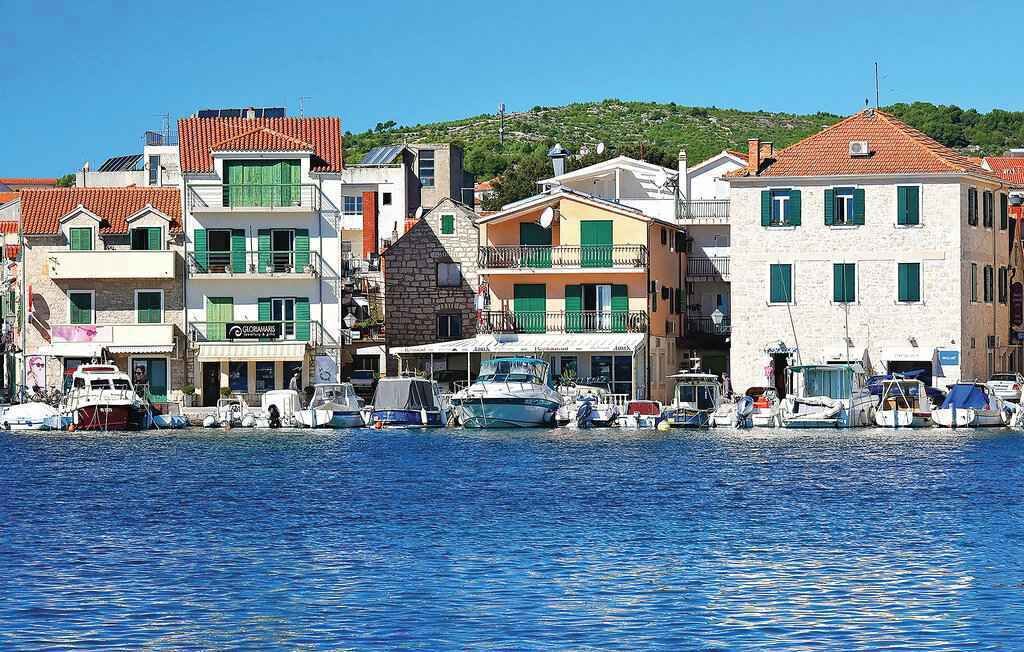 Eine Küstenstadt mit Gebäuden entlang der Uferpromenade, wo Boote vor Anker liegen, und ein klarer, blauer Himmel.