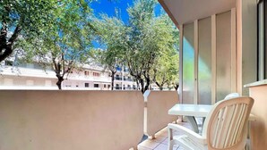 Uma varanda com mesa e cadeiras, uma janela com persianas e vista para edifícios e árvores.