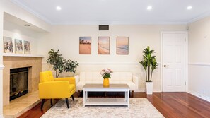 A living room with a fireplace, yellow armchairs, a white sofa, a coffee table, and a door. - Twilight Terrace by Avantstay West Hills Retreat Hot Tub, BBQ + EV Charger, Near Malibu (West Hills)