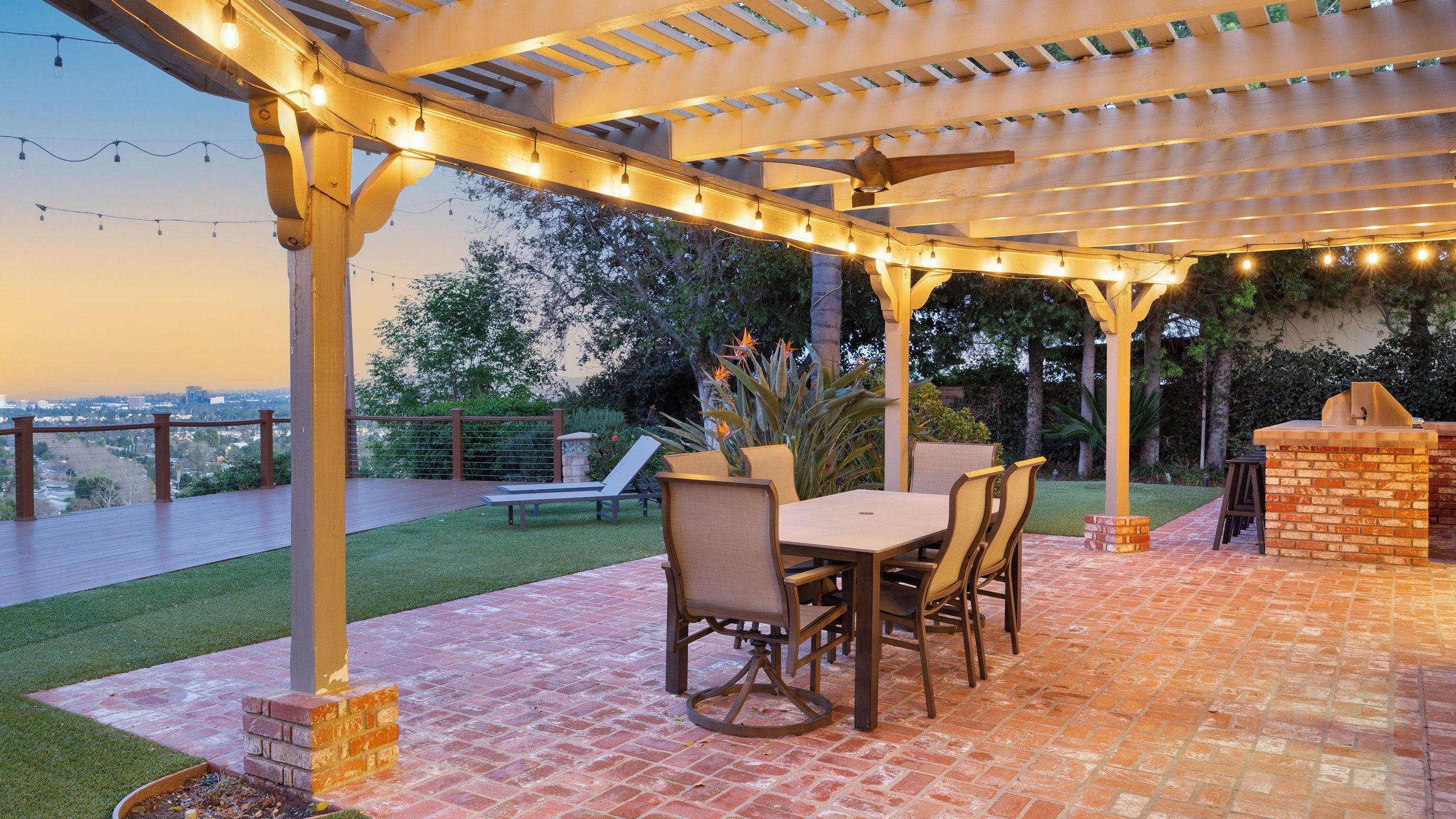 Eine Terrasse im Freien mit einer Pergola, Lichterketten, einem gemauerten Grill und Blick auf die Stadt.