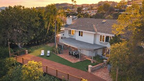 Ein zweistöckiges Haus mit einer Terrasse, einer überdachten Sitzgelegenheit und Blick auf die umliegende Landschaft.