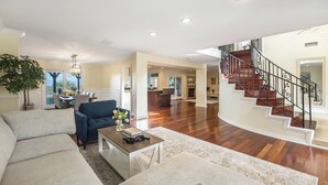 A spacious living area with a sofa, coffee table, and a dining table. A staircase with a railing leads to an upper floor. - Twilight Terrace by Avantstay West Hills Retreat Hot Tub, BBQ + EV Charger, Near Malibu (West Hills)