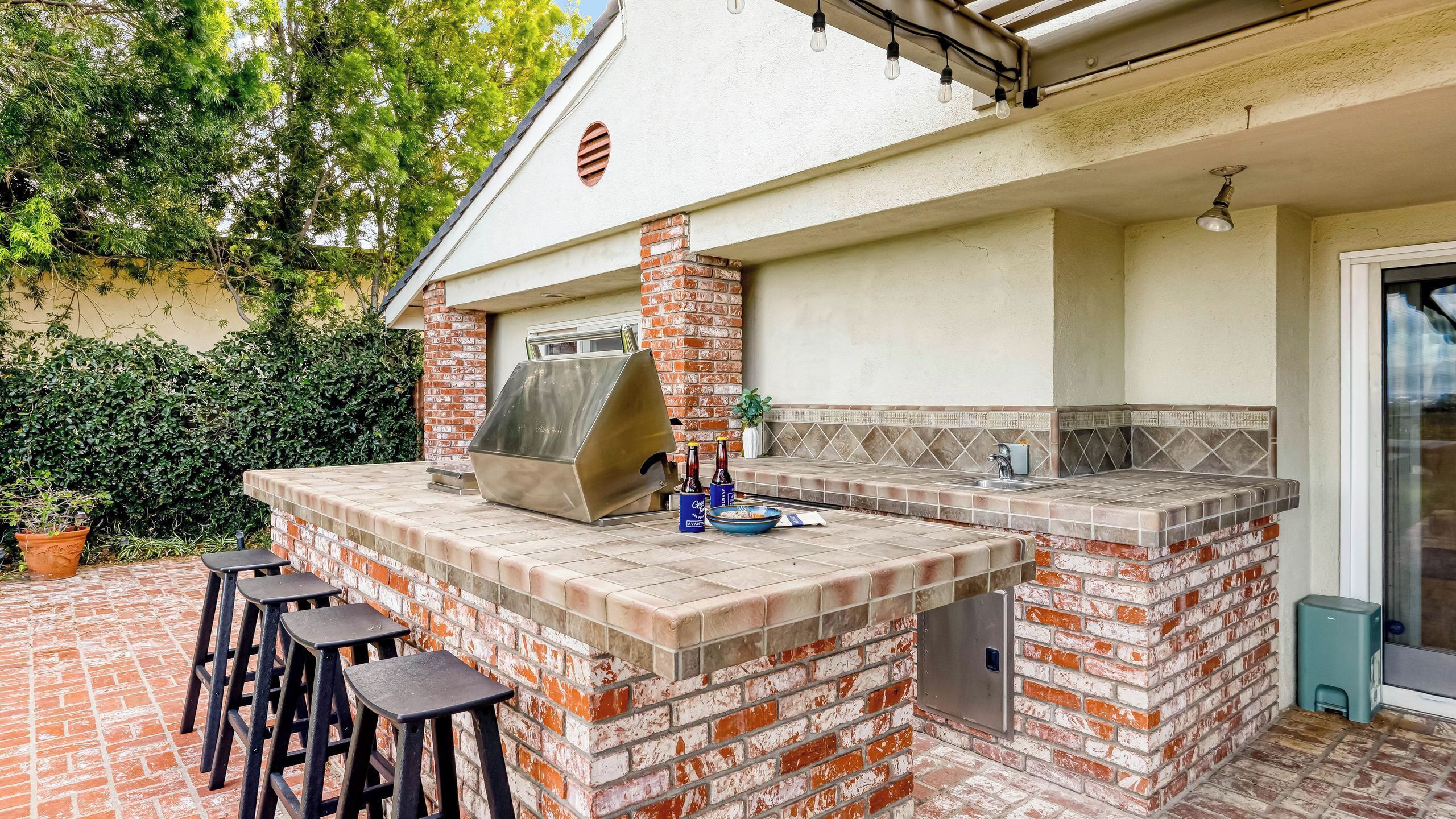 An outdoor kitchen with a grill, bar stools, and a tiled backsplash.