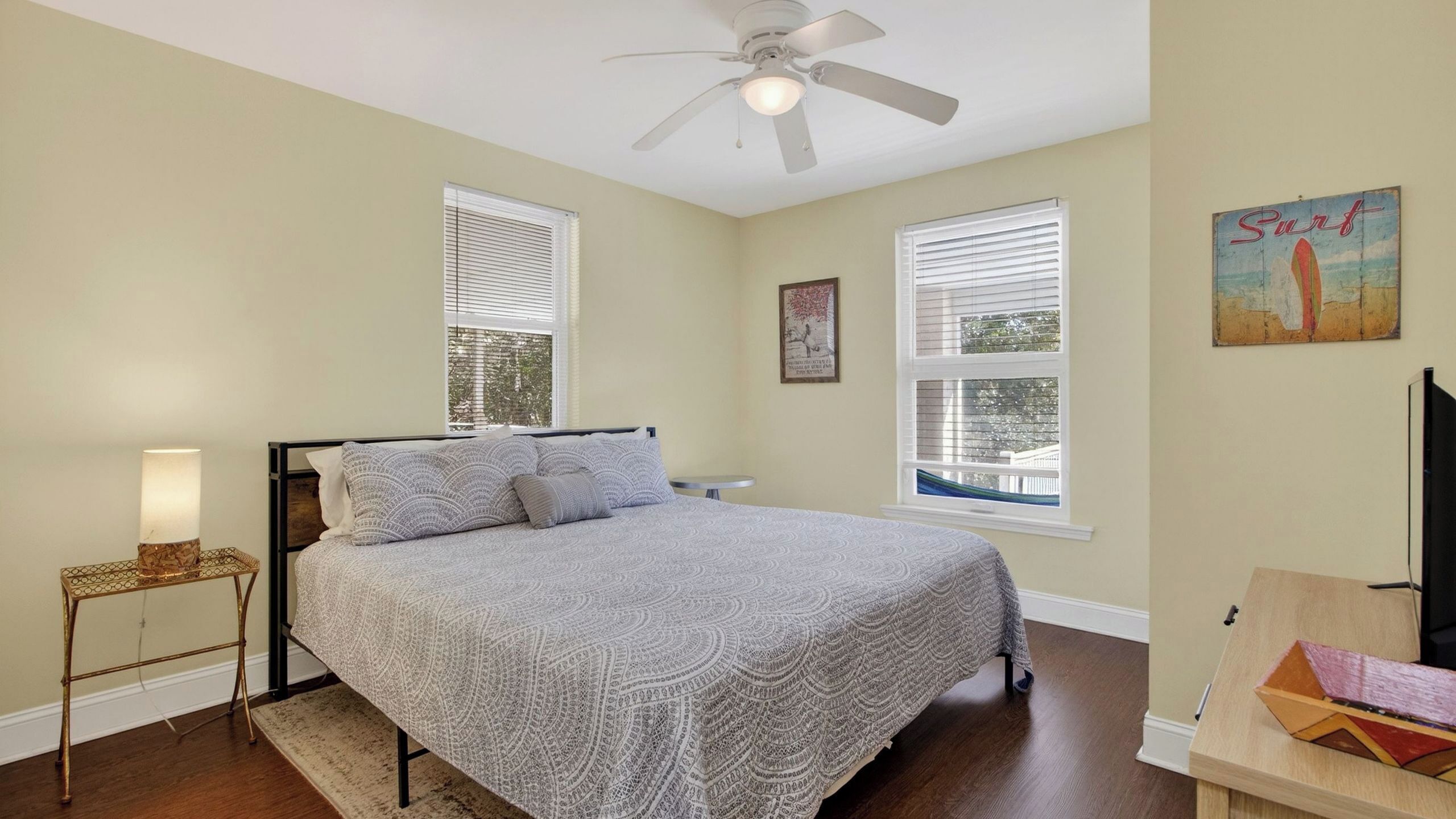 A bedroom with a bed, a standing lamp, a ceiling fan, and two windows with blinds.