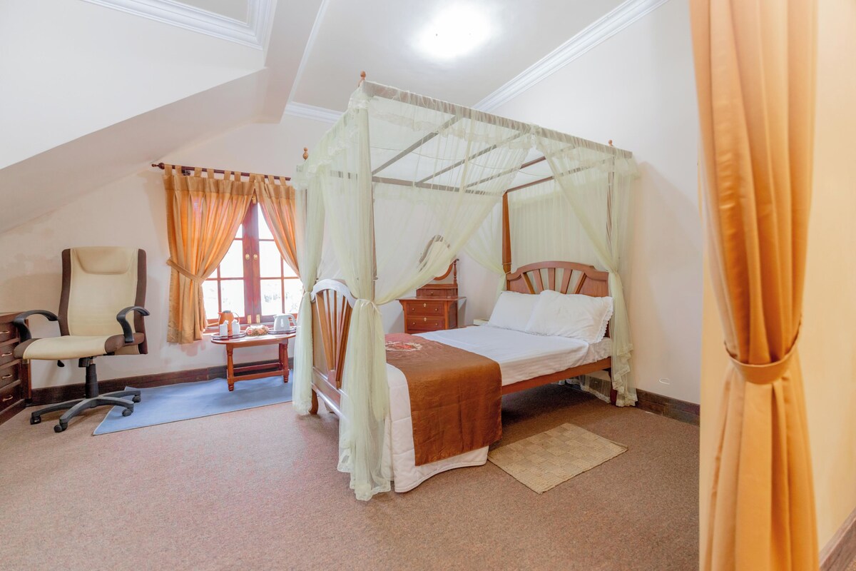 A bedroom with a four-poster bed, a desk with a chair, and a window with curtains.