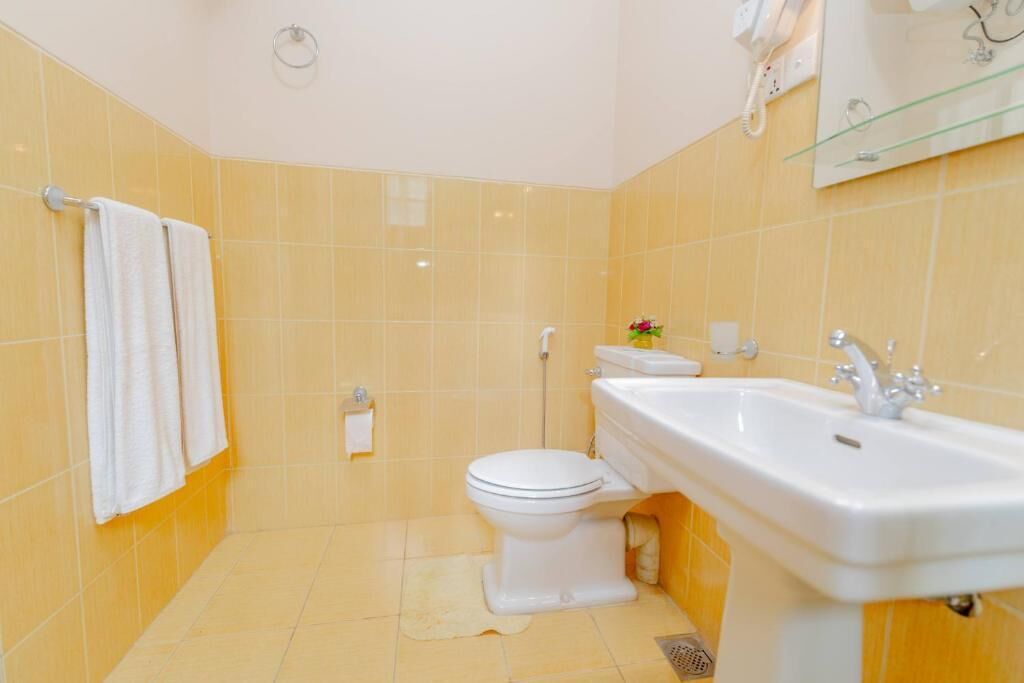 A bathroom with yellow tiles, a white sink, a toilet, and a towel rack with two towels.