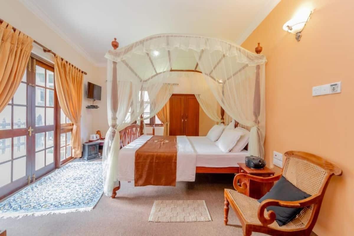 Ein Schlafzimmer mit einem Himmelbett, einem Holzstuhl, einem Nachttisch und einem großen Fenster mit Vorhängen.