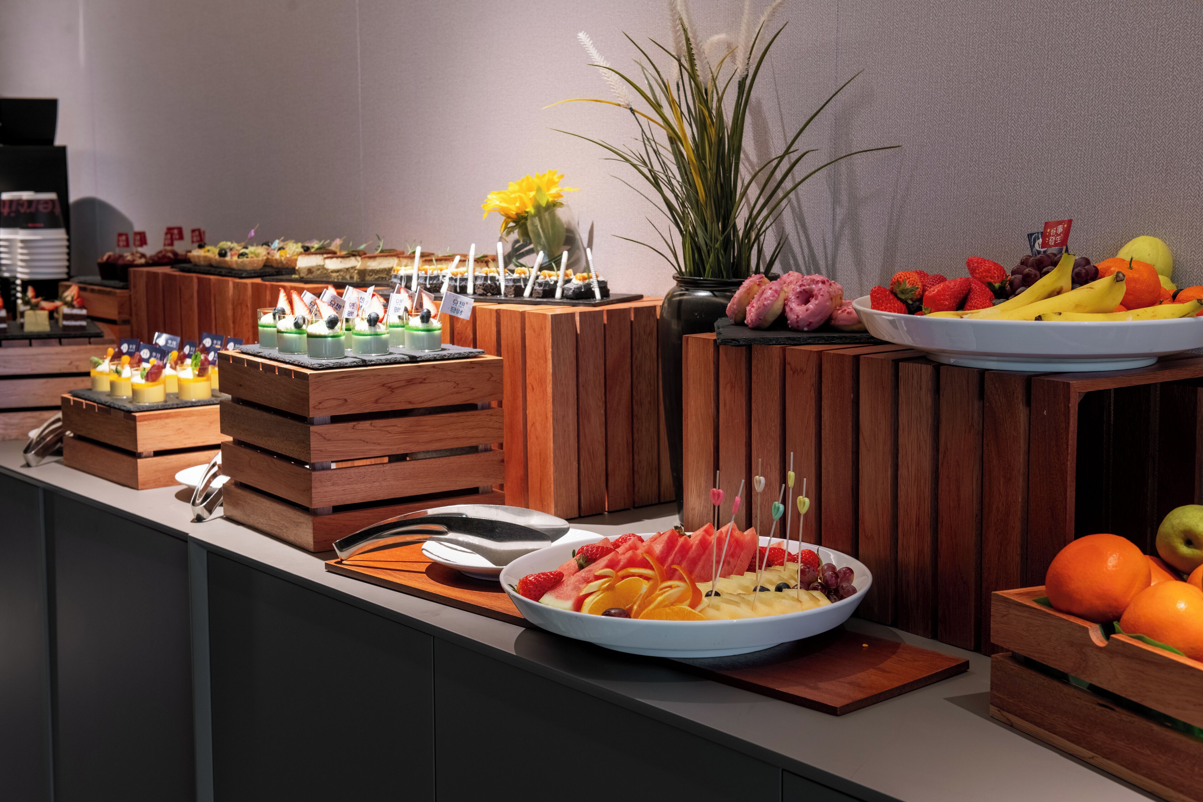 Disposição de buffet com diversos alimentos e uma planta decorativa.