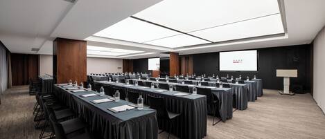 A conference room with long tables, chairs, and a projector screen.