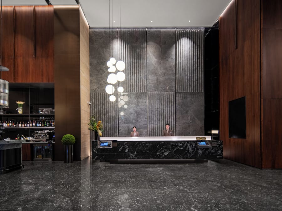 Una reception con scrivania e display digitale, un'area bar con bottiglie e una parete decorativa con linee verticali.