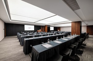 A conference room with long tables, chairs, a projector screen, and a large window.