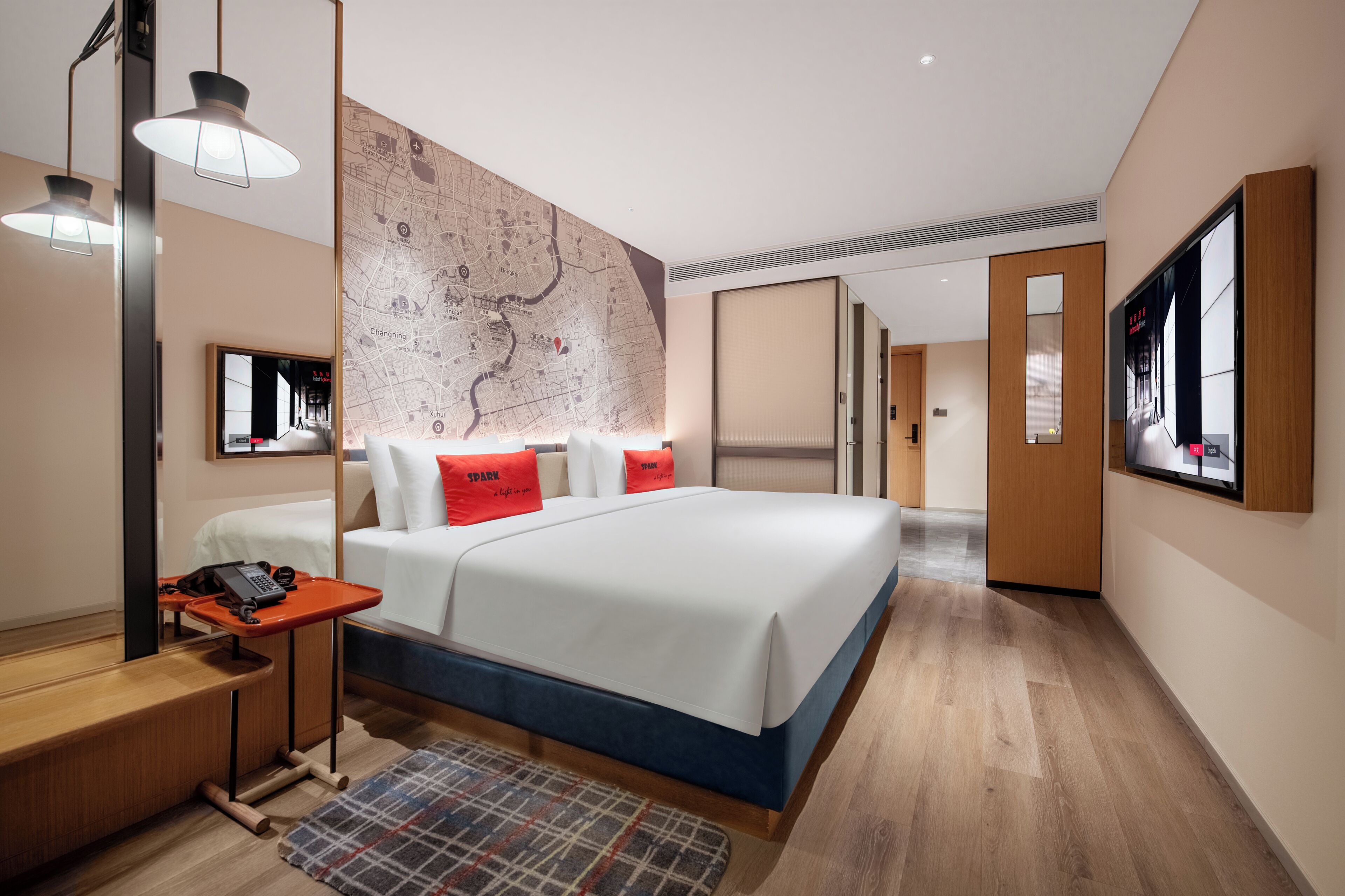 A modern hotel room with a large bed, a map on the wall, a desk with a phone, and a TV on the wall.