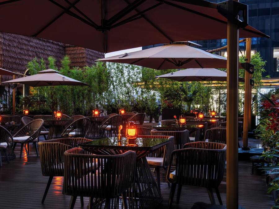 An outdoor dining area with tables and chairs, umbrellas, and lanterns.