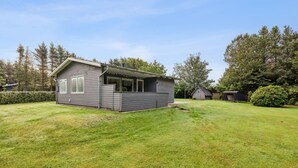 Ett litet hus i ett våningsplan med en inglasad veranda och en välskött gräsmatta.