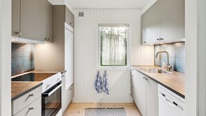 Ett kompakt kök med vita skåp, en inbyggd ugn, en diskho och ett fönster med utsikt över träd.