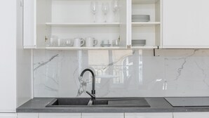 Cozinha com armários brancos, painel de fundo de mármore e pia preta.