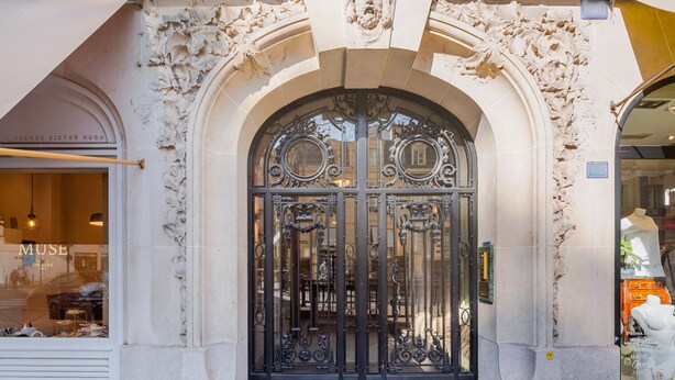 Entrada de edifício com portões de ferro ornamentados e fachada de pedra.
