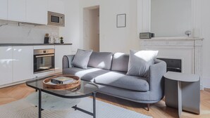 Uma sala de estar moderna com um sofá cinzento, uma mesa de centro de vidro e uma lareira.
