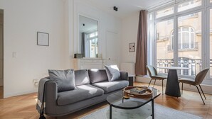 Uma sala de estar moderna com um sofá cinzento, uma mesa de centro de vidro e vista para uma varanda com mobiliário exterior.