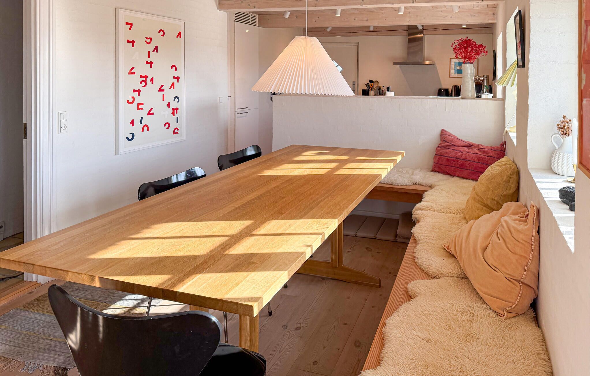 A modern dining area with a wooden table, black chairs, a sofa with cushions, and a hanging light fixture.