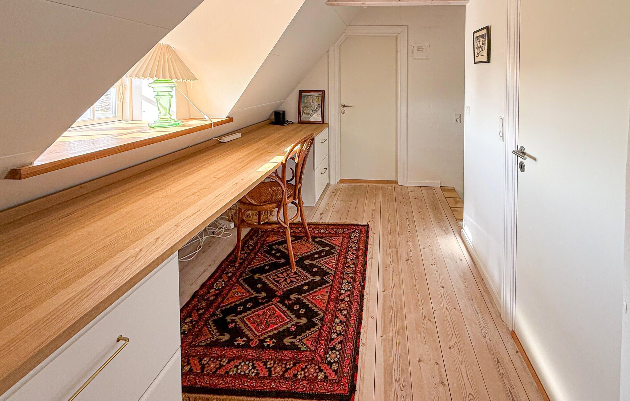 A narrow hallway with a wooden bench and a patterned rug, leading to a door.